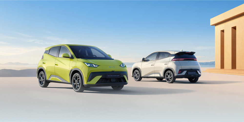 Two BYD Dolphin Surfs parked in a desert with a modern-looking building on the right